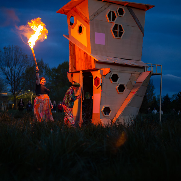 woman with lit torch nears the 2024 Built to Burn structure with assistant professor Totem Shriver