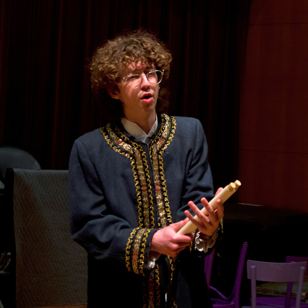 Student dressed in gold and black formal shirt performs a song.