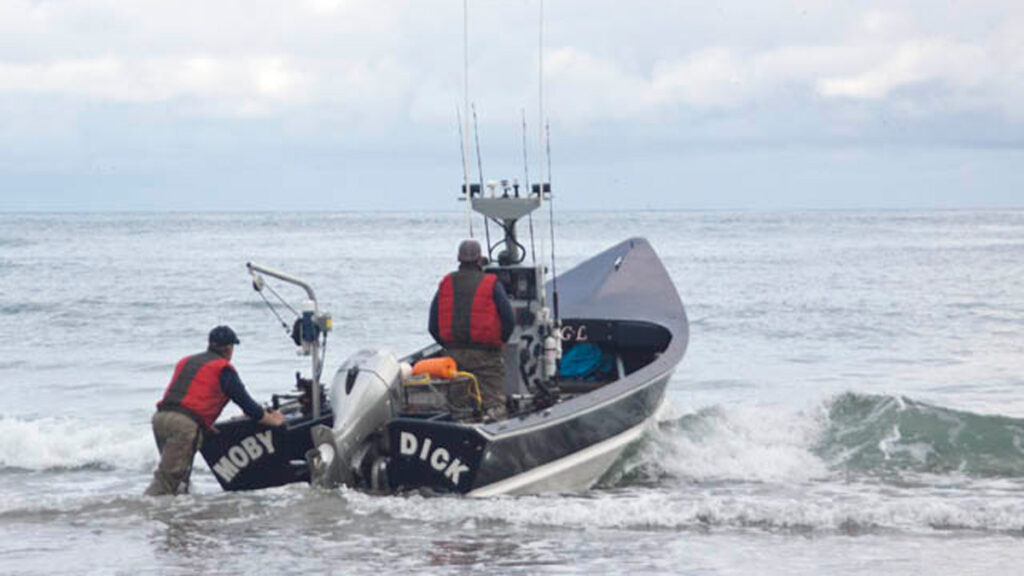 Fisherman pushes out a dory boat into the ocean. Boat name is "Moby Dick". Photo by Ty Marshall.