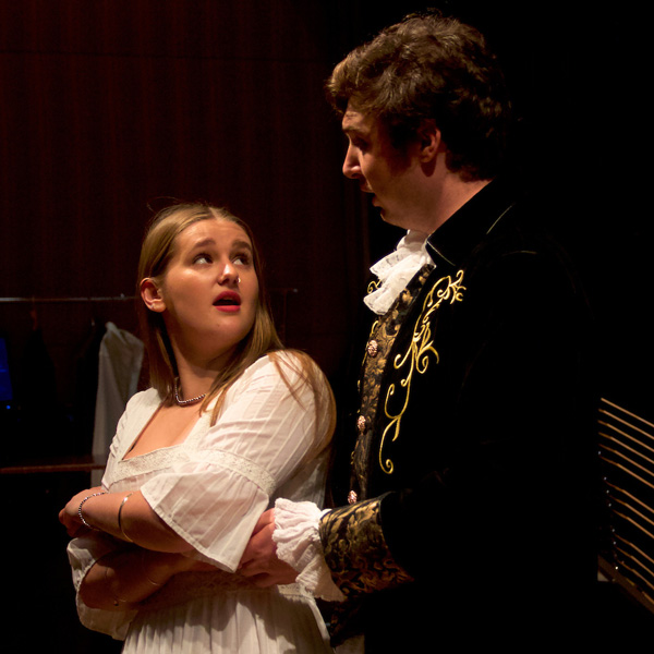Male and female student in dress costumes sing facing each other