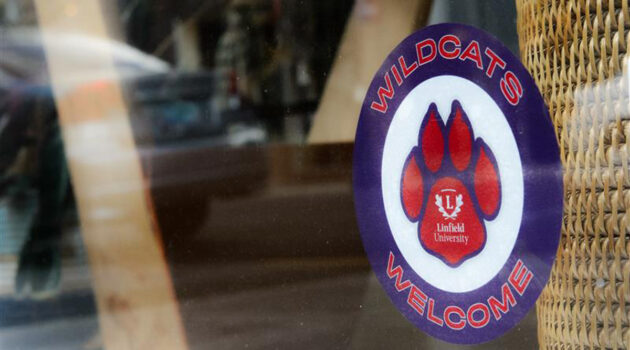 A Cats Community Partner sticker is displayed in a business window.The sticker is a purple circle reading Wildcats Welcome. The interior of the sticker has a red and purple paw on a white background with the Linfield logo.