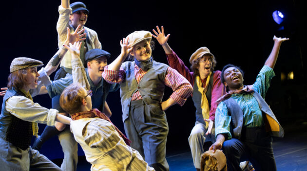 Group of dancers in costumes pose at the end of a dance