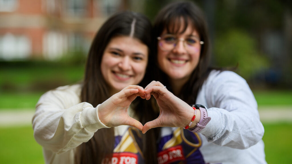 Two students wearing Wild for Linfield shirts make a heart with their hands