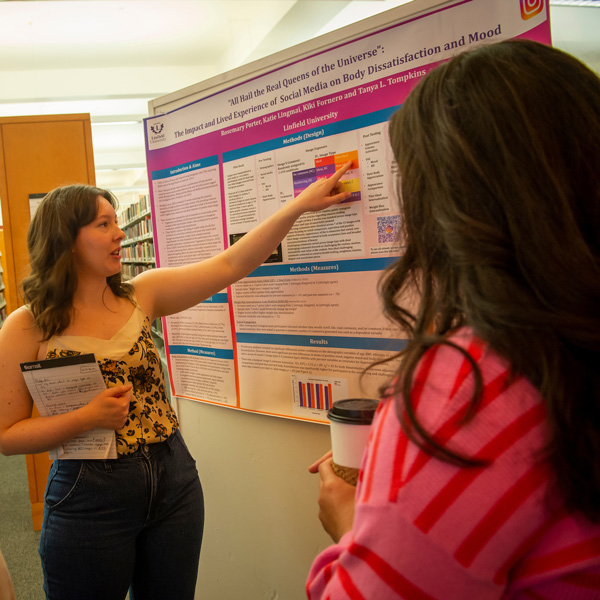 A student points to her poster, explaining her research, to a guest