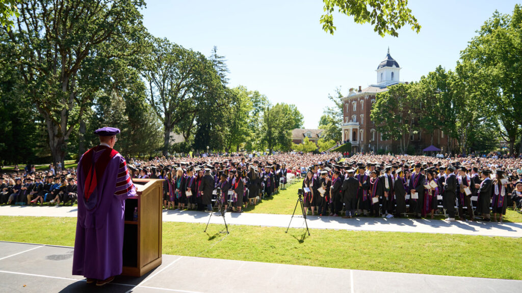 President Mark Blegen stands in front a packed crowd of graduates and family members at Commencement