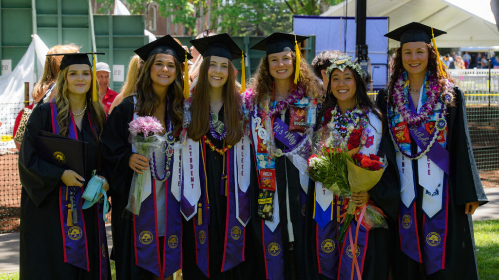 group of female graduates wearing regalia and holding degrees and flowers