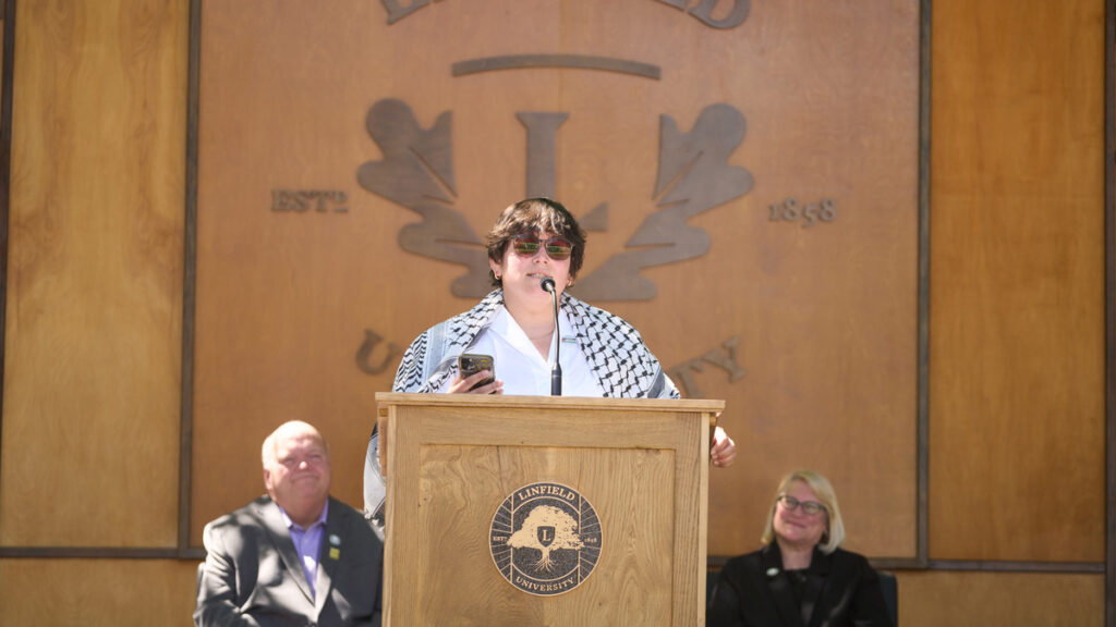 Jess McGough reads a speech at the podium with Dean Paul Smith and Associate Dean Julie Fitzwater in the background