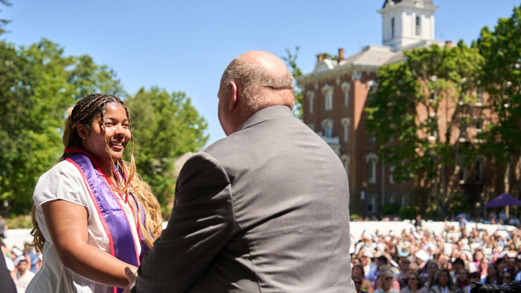 Dean Paul Smith shakes the hand of. a nursing student in front of a crowd of guests.