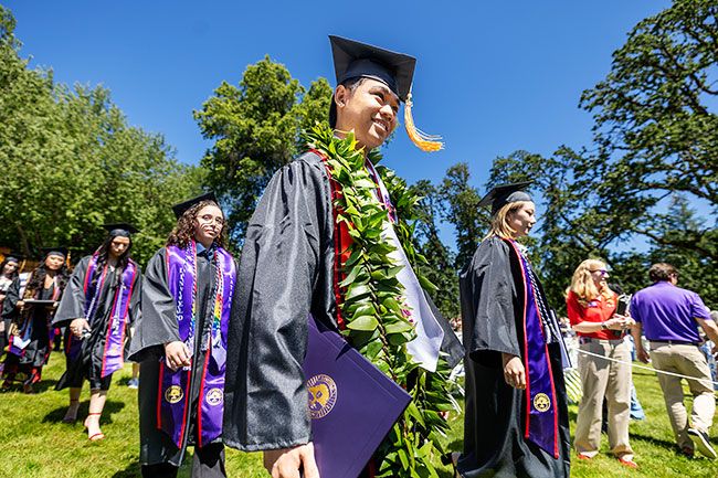 Linfield graduates in full regalia walk in a line from the venue